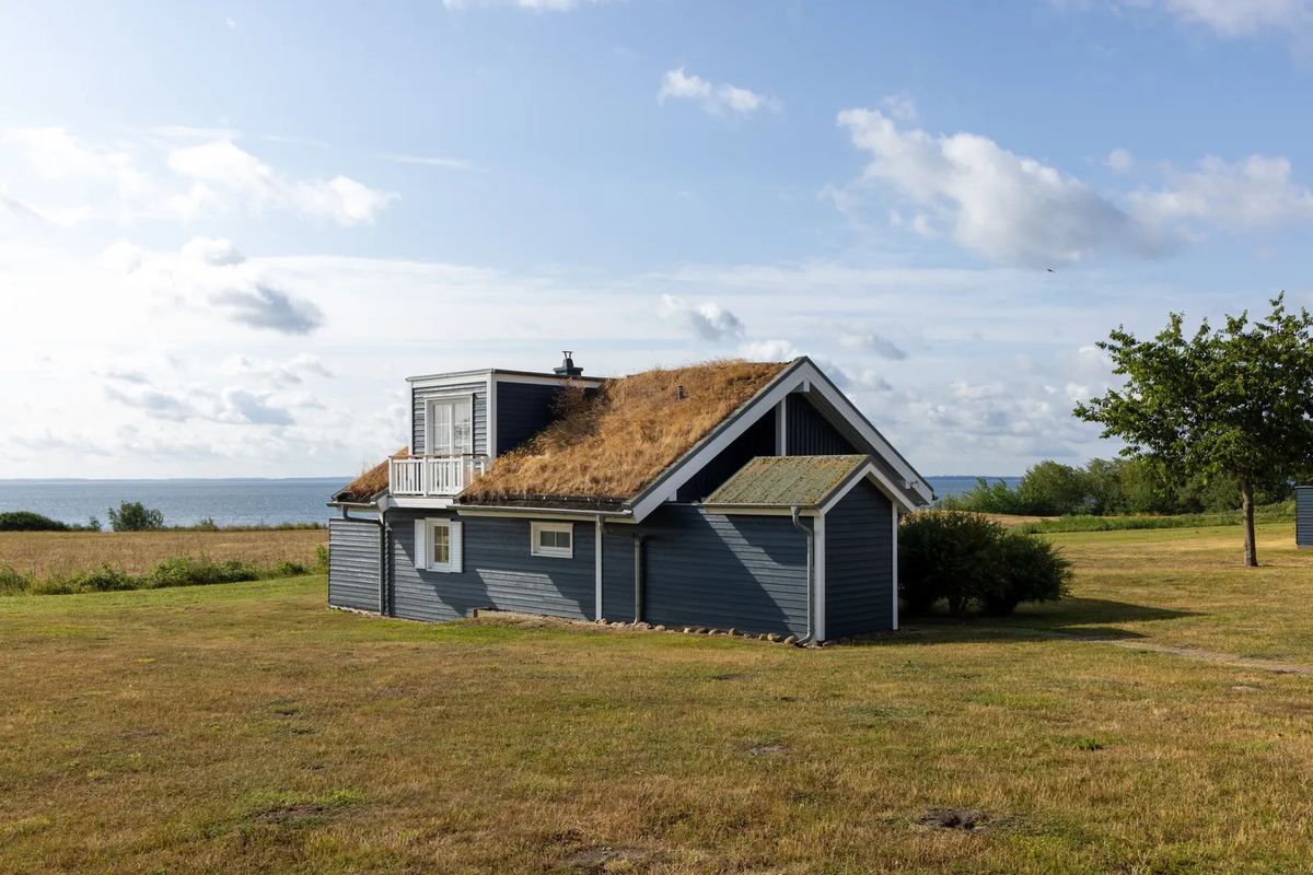 Kleines Haus mit Grasdach, dahinter das Meer