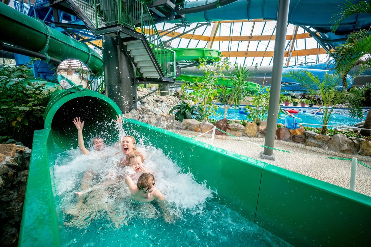 Kinder rutschen in einer grünen Rutsche ins Wasser