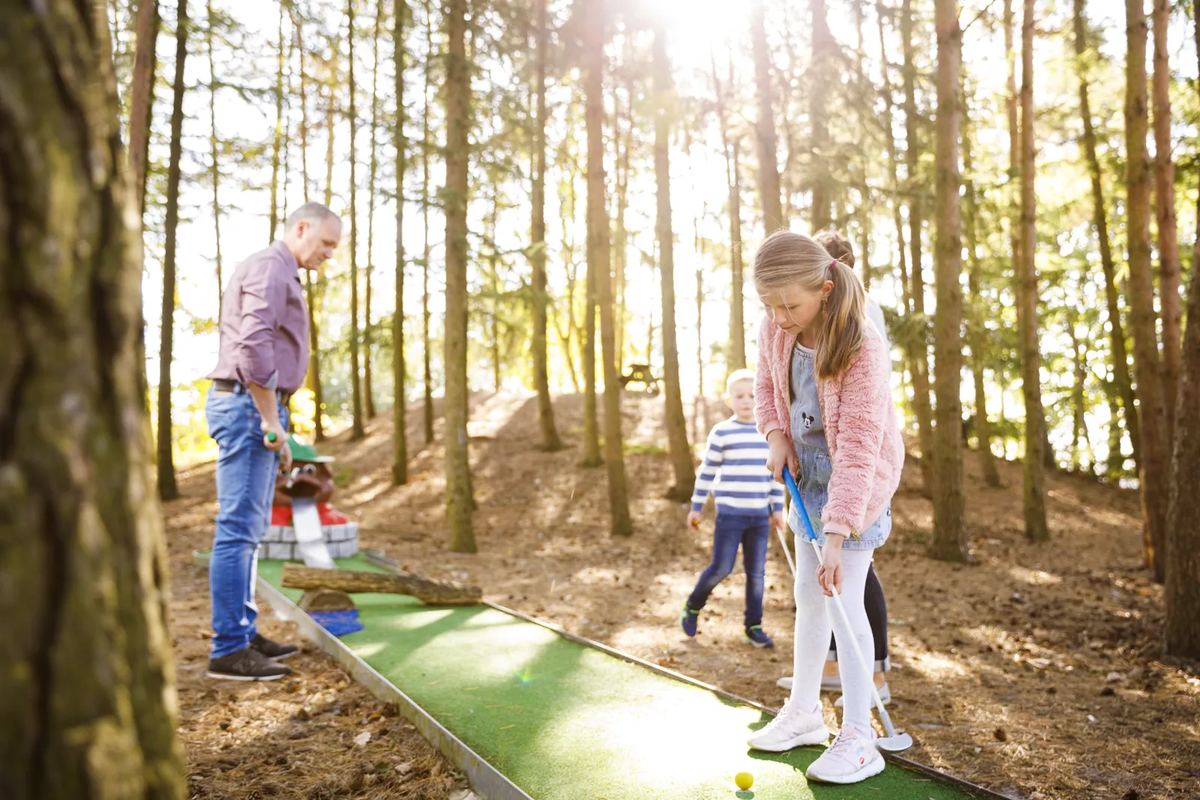 Familie spielt Minigolf zwischen Kiefern