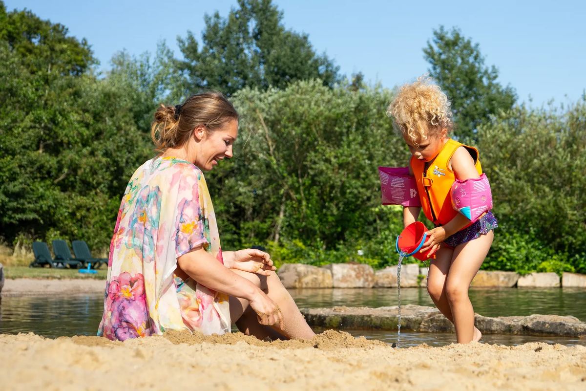 Kind mit Schwimmflügeln spielt im Sand am Wasser