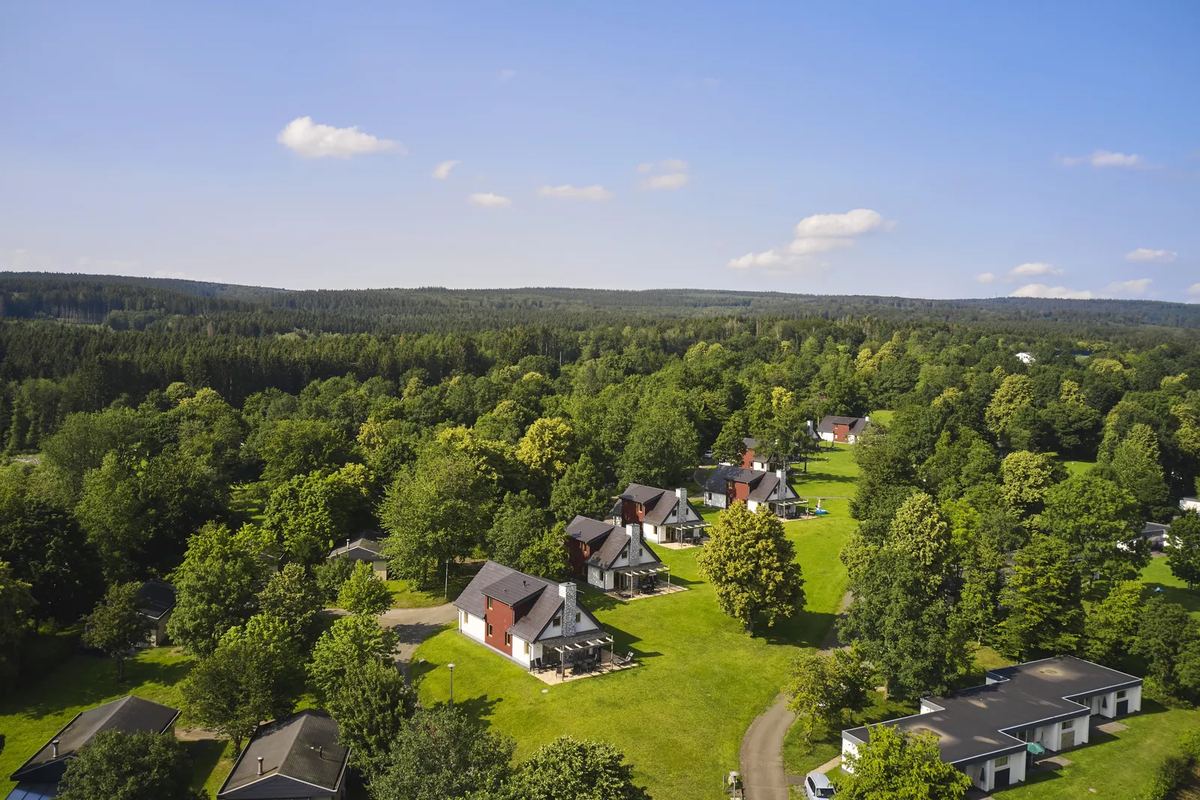 Luftbild: Ferienhäuser zwischen Bäumen, dahinter Wald