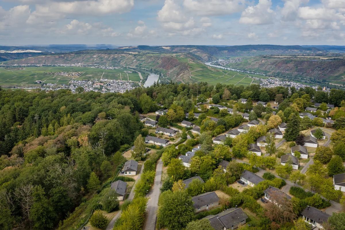 Luftbild: Ferienhäuser im Wald, dahinter ein breites Tal