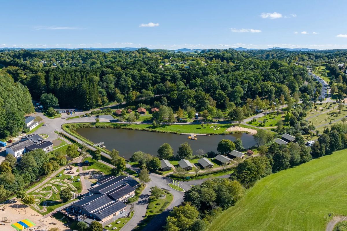 Luftbild: Park mit Teich, Wiesen und Ferienhäusern zwischen bewaldeten Hügeln