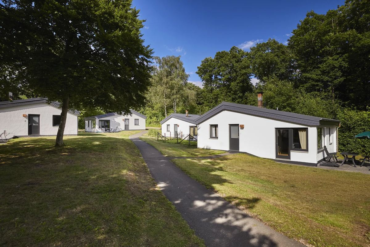 Weiße Bungalows an einem Weg zwischen Bäumen
